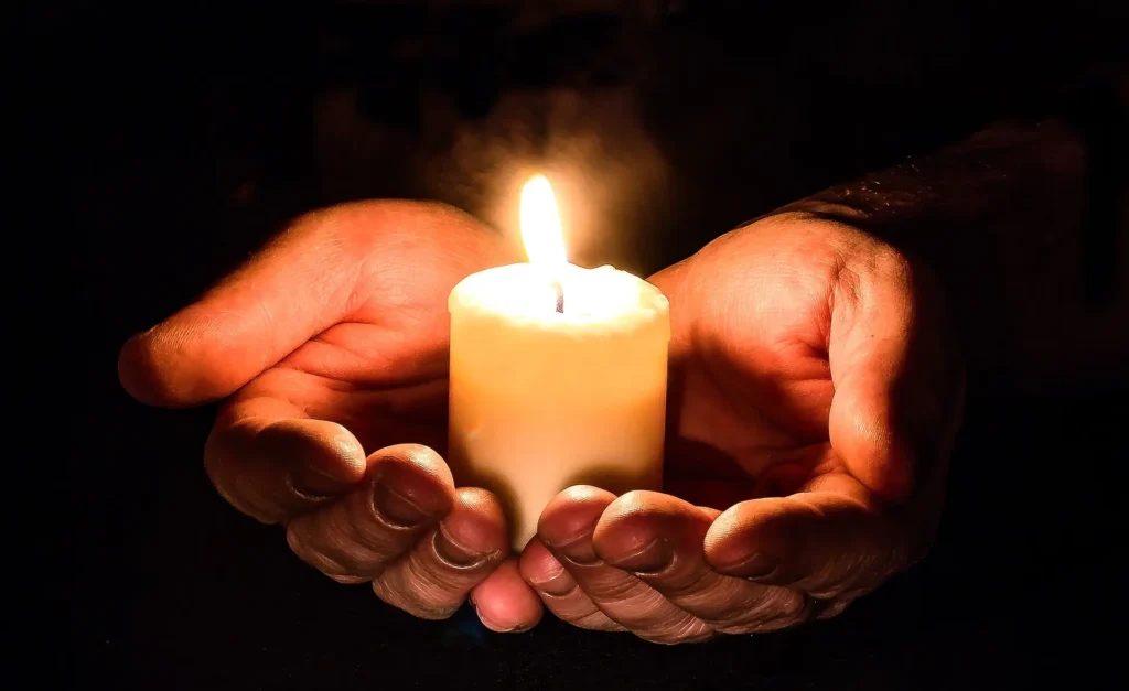 A pair of hands holding a lit cannabis-infused candle