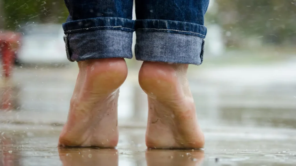 A man in jeans, brave enough to go barefoot on a rainy street, having used urea in skincare foot products