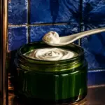 Dark emerald jar of white cream with a porcelain spatula, cobalt blue tiles, copper shelf and cannabis leaf shadow. Text reads: Better Cannabis Topicals, Cetearyl Alcohol, 420formulator.com.